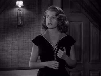 Movie still from “Affair in Trinidad” (1952), directed by Vincent Sherman – A black and white photo of a woman holding a phone; Medium shot, Over the shoulder angle