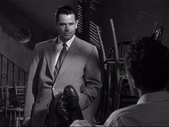 Movie still from “Affair in Trinidad” (1952), directed by Vincent Sherman – A black and white photo of a man in a suit and tie; Medium shot, Over the shoulder angle