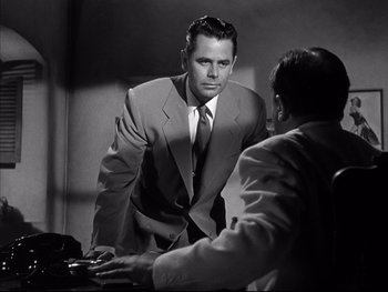 Movie still from “Affair in Trinidad” (1952), directed by Vincent Sherman – A man wearing a suit and tie talking to another man; Medium shot, Over the shoulder angle