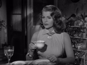Movie still from “Affair in Trinidad” (1952), directed by Vincent Sherman – A woman sitting at a table with a cup of tea; Medium shot, Over the shoulder angle