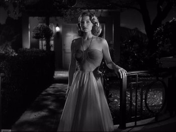 Movie still from “Affair in Trinidad” (1952), directed by Vincent Sherman – A woman in a long dress standing in front of a railing; Medium shot, Low angle