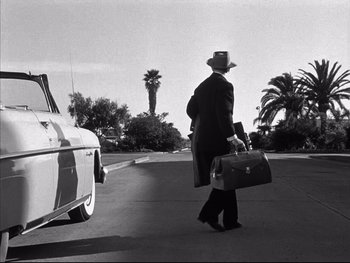 Movie still from “Affair in Trinidad” (1952), directed by Vincent Sherman – A black and white photo of a man walking down the street with a suit case; Wide shot, Low angle