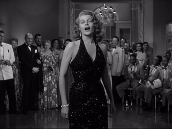 Movie still from “Affair in Trinidad” (1952), directed by Vincent Sherman – A black and white photo of a woman singing; Medium shot, Low angle