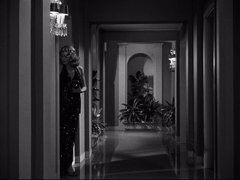 Movie still from “Affair in Trinidad” (1952), directed by Vincent Sherman – A woman is standing in a hallway holding a camera; Wide shot, Low angle