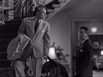 Movie still from “Affair in Trinidad” (1952), directed by Vincent Sherman – A man in a suit standing next to another man in a suit; Medium shot, Low angle