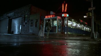 Movie still from “After Hours” (1985), directed by Martin Scorsese – Two people walking on the sidewalk at night near a bus stop; Wide shot, High angle
