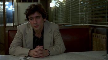 Movie still from “After Hours” (1985), directed by Martin Scorsese – A man sitting at a table with his hands crossed; Close Up shot, Over the shoulder angle