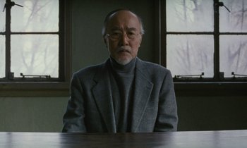 Movie still from “After Life” (1998), directed by Kore-eda Hirokazu – An older man sitting at a table in front of a window; Medium shot, Low angle