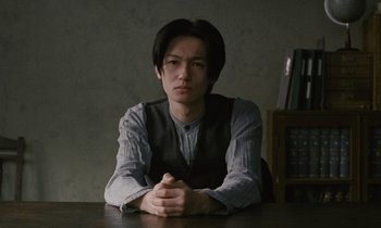 Movie still from “After Life” (1998), directed by Kore-eda Hirokazu – A man sitting at a table in front of books; Medium shot, Low angle