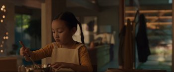 Movie still from “After Yang” (2021), directed by Kogonada – A young girl in an apron looking down at a piece of paper; Medium shot, Over the shoulder angle