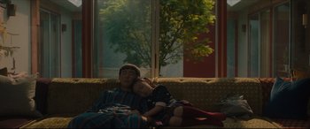 Movie still from “After Yang” (2021), directed by Kogonada – A man and a child laying on a couch in front of a window; Medium shot, High angle