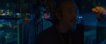Movie still from “After Yang” (2021), directed by Kogonada – A man standing next to another man in a dark room; Medium shot, Over the shoulder angle