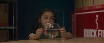 Movie still from “After Yang” (2021), directed by Kogonada – A little girl is holding a fish bowl in front of her face; Close Up shot, High angle