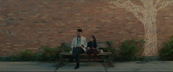 Movie still from “After Yang” (2021), directed by Kogonada – A man sitting on top of a wooden bench next to a little girl; Wide shot, High angle