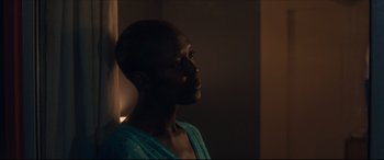 Movie still from “After Yang” (2021), directed by Kogonada – A woman is looking out a window at the light; Close Up shot, Over the shoulder angle