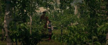 Movie still from “After Yang” (2021), directed by Kogonada – Two people standing in an apple orchard looking at each other; Wide shot, Over the shoulder angle