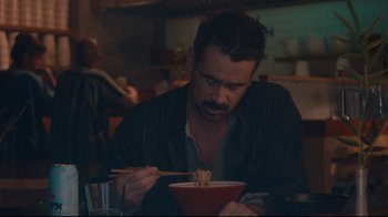 Movie still from “After Yang” (2021), directed by Kogonada – A man sitting at a table with chopsticks in front of a bowl of food; Medium shot, Over the shoulder angle