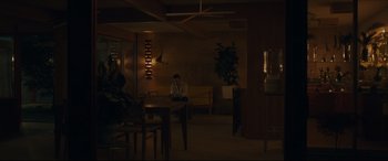 Movie still from “After Yang” (2021), directed by Kogonada – A man sitting at a table in a dark room; Extreme Wide shot, Over the shoulder angle
