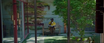 Movie still from “After Yang” (2021), directed by Kogonada – A woman sitting on a bench reading a book; Wide shot, High angle