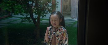 Movie still from “After Yang” (2021), directed by Kogonada – A little girl standing in front of a tree and building; Medium shot, High angle