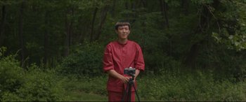 Movie still from “After Yang” (2021), directed by Kogonada – A man holding a camera in front of a forest; Medium shot, Low angle
