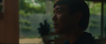 Movie still from “After Yang” (2021), directed by Kogonada – A young man looking out of a window at the trees; Close Up shot, Low angle