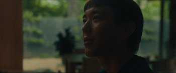 Movie still from “After Yang” (2021), directed by Kogonada – A young asian man is looking into the distance; Close Up shot, Low angle