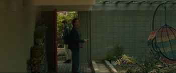 Movie still from “After Yang” (2021), directed by Kogonada – A man standing in front of a building holding a remote control; Wide shot, Low angle