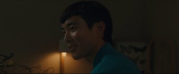 Movie still from “After Yang” (2021), directed by Kogonada – A young man smiling for the camera in the dark; Close Up shot, Over the shoulder angle