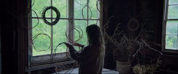 Movie still from “After Yang” (2021), directed by Kogonada – A woman standing in front of a large window with wreaths hanging from it; Medium shot, Over the shoulder angle