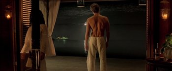 Movie still from “After the Sunset” (2004), directed by Brett Ratner – A shirtless man standing in front of a body of water at night; Wide shot, Over the shoulder angle
