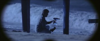 Movie still from “After the Sunset” (2004), directed by Brett Ratner – A man is holding a flashlight and a camera; Wide shot, Low angle