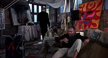 Movie still from “Age of Consent” (1969), directed by Michael Powell – A man sitting on a chair in a room; Wide shot, Low angle