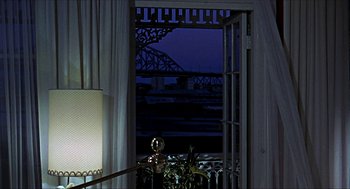 Movie still from “Age of Consent” (1969), directed by Michael Powell – A view of a bridge through a window at night; Extreme Wide shot, Over the shoulder angle