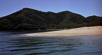 Movie still from “Age of Consent” (1969), directed by Michael Powell – A view of a beach with a mountain in the background; Extreme Wide shot, High angle