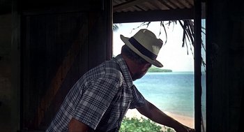 Movie still from “Age of Consent” (1969), directed by Michael Powell – A man wearing a hat looking out of a window; Medium shot, Low angle