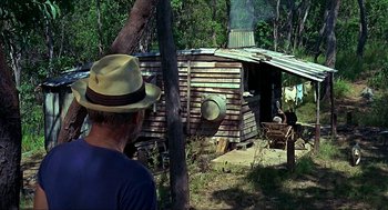 Movie still from “Age of Consent” (1969), directed by Michael Powell – A man wearing a straw hat looking at an outhouse in the woods; Wide shot, Over the shoulder angle