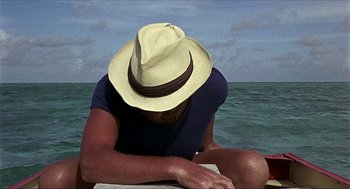Movie still from “Age of Consent” (1969), directed by Michael Powell – A man sitting on the beach wearing a straw hat; Close Up shot, Overhead angle