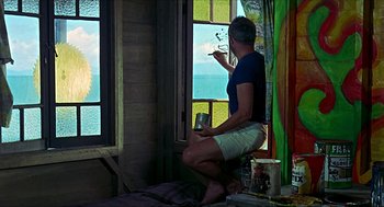 Movie still from “Age of Consent” (1969), directed by Michael Powell – A man sitting on the ground painting a window; Wide shot, Low angle