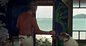Movie still from “Age of Consent” (1969), directed by Michael Powell – A man standing in front of a window looking out at the ocean; Medium shot, Low angle