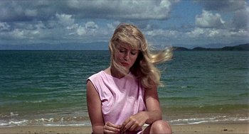 Movie still from “Age of Consent” (1969), directed by Michael Powell – A woman sitting on the beach looking at her watch; Medium shot, Low angle