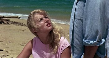 Movie still from “Age of Consent” (1969), directed by Michael Powell – A woman sitting on the beach with a man standing next to her; Close Up shot, Low angle