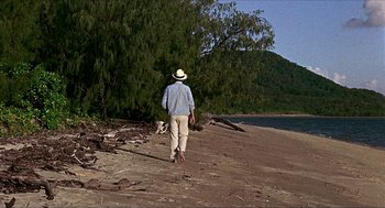 Movie still from “Age of Consent” (1969), directed by Michael Powell – A man walking on the beach with a hat on his head; Extreme Wide shot, High angle