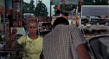 Movie still from “Age of Consent” (1969), directed by Michael Powell – A woman standing next to a man in a store; Medium shot, Over the shoulder angle