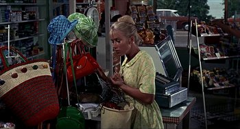 Movie still from “Age of Consent” (1969), directed by Michael Powell – A woman is looking at a bag in a store; Medium shot, High angle