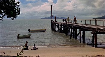 Movie still from “Age of Consent” (1969), directed by Michael Powell – A group of people sitting on a pier near the ocean; Extreme Wide shot, High angle