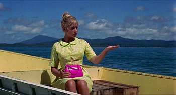 Movie still from “Age of Consent” (1969), directed by Michael Powell – A woman sitting in a boat on the water holding a pink purse; Medium shot, Low angle