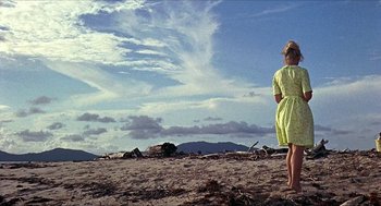 Movie still from “Age of Consent” (1969), directed by Michael Powell – A woman in a yellow dress standing on a beach; Extreme Wide shot, Low angle