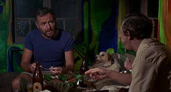 Movie still from “Age of Consent” (1969), directed by Michael Powell – Two men sitting at a dinner table with a dog; Medium shot, Over the shoulder angle