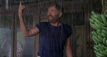 Movie still from “Age of Consent” (1969), directed by Michael Powell – A man standing in the pouring rain holding his arm up; Medium shot, Low angle